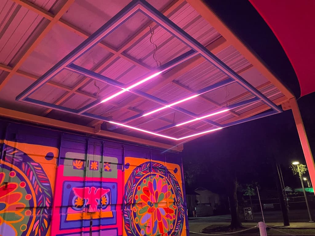 Pink-lit linear grid against the dark sky from a lower angle, mural visible behind.