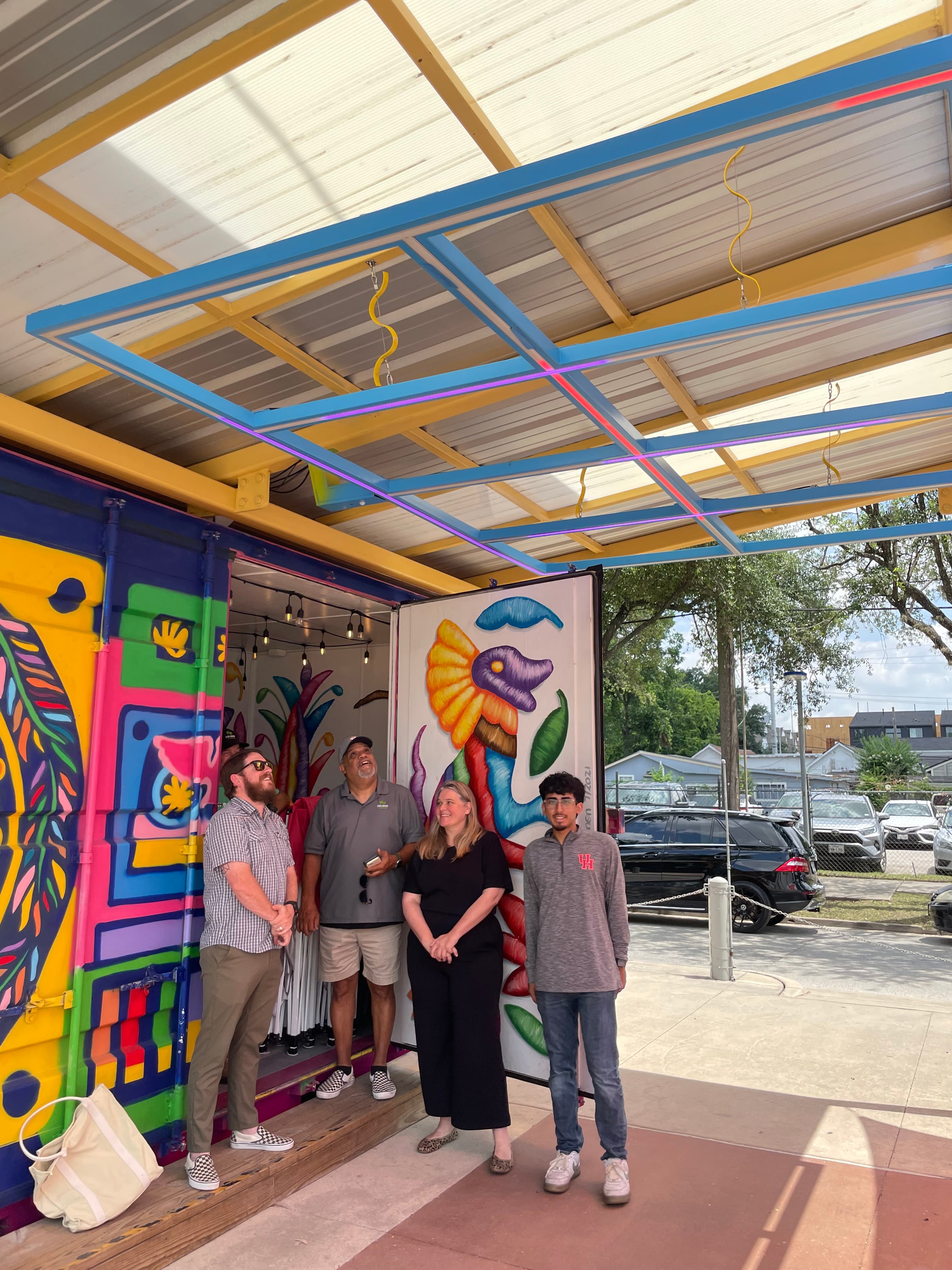 A group gathered at Esplanade in front of a vivid mural, the outdoor space lived-in and animated.