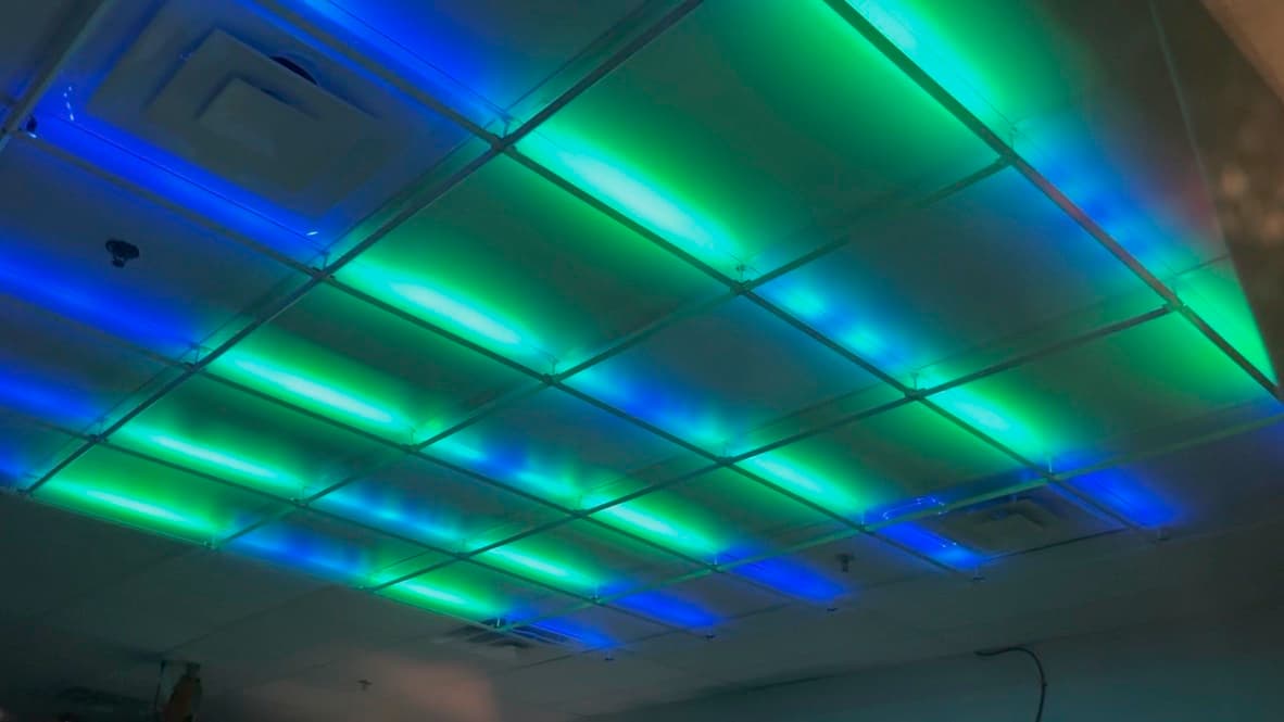 Popston’s overhead drop-ceiling lighting in a saturated blue-and-green wash, light bouncing off the panels.