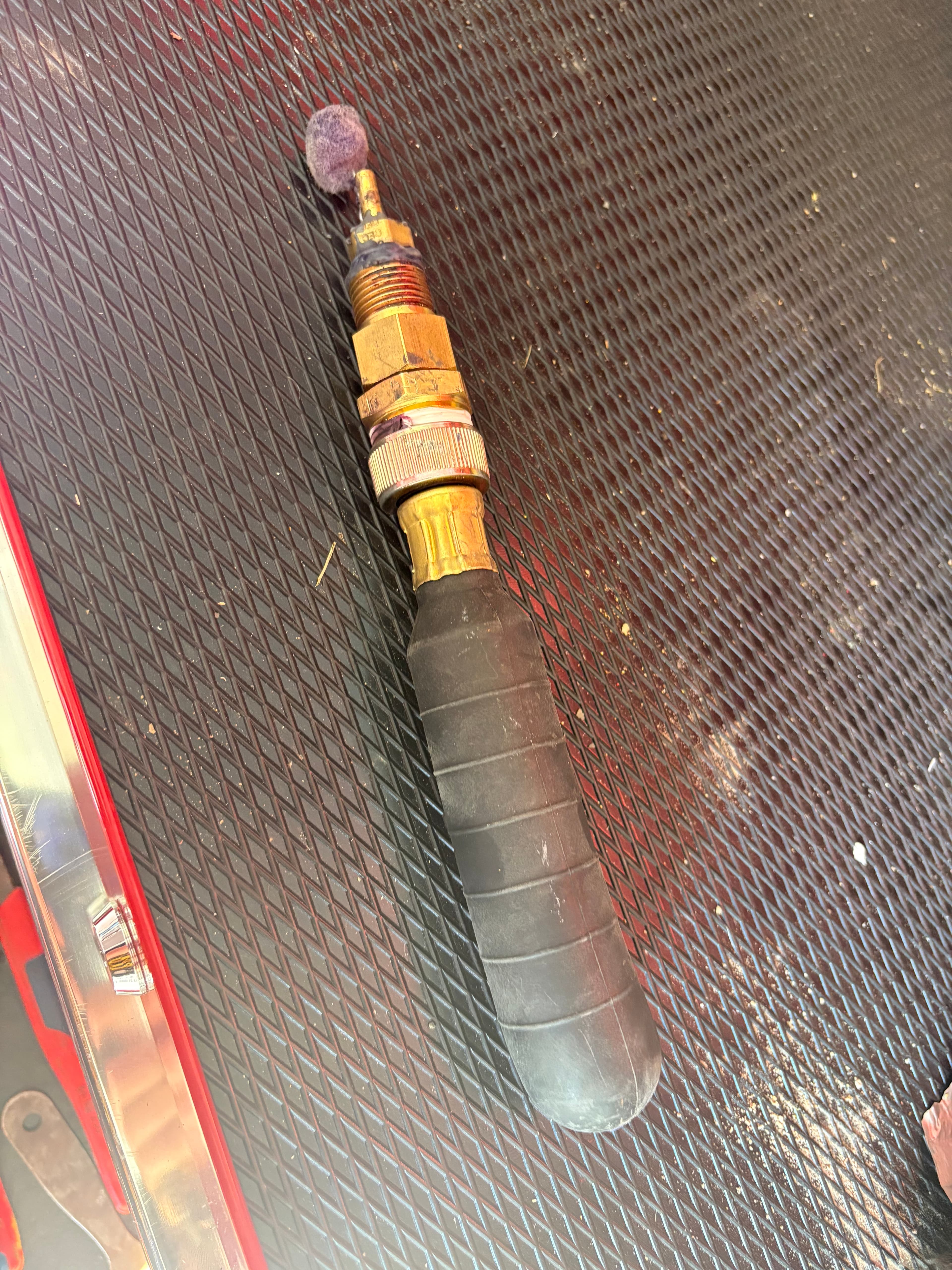 The earliest Primer Wand prototype — black rubber bulb and brass fittings on a red metal workbench.