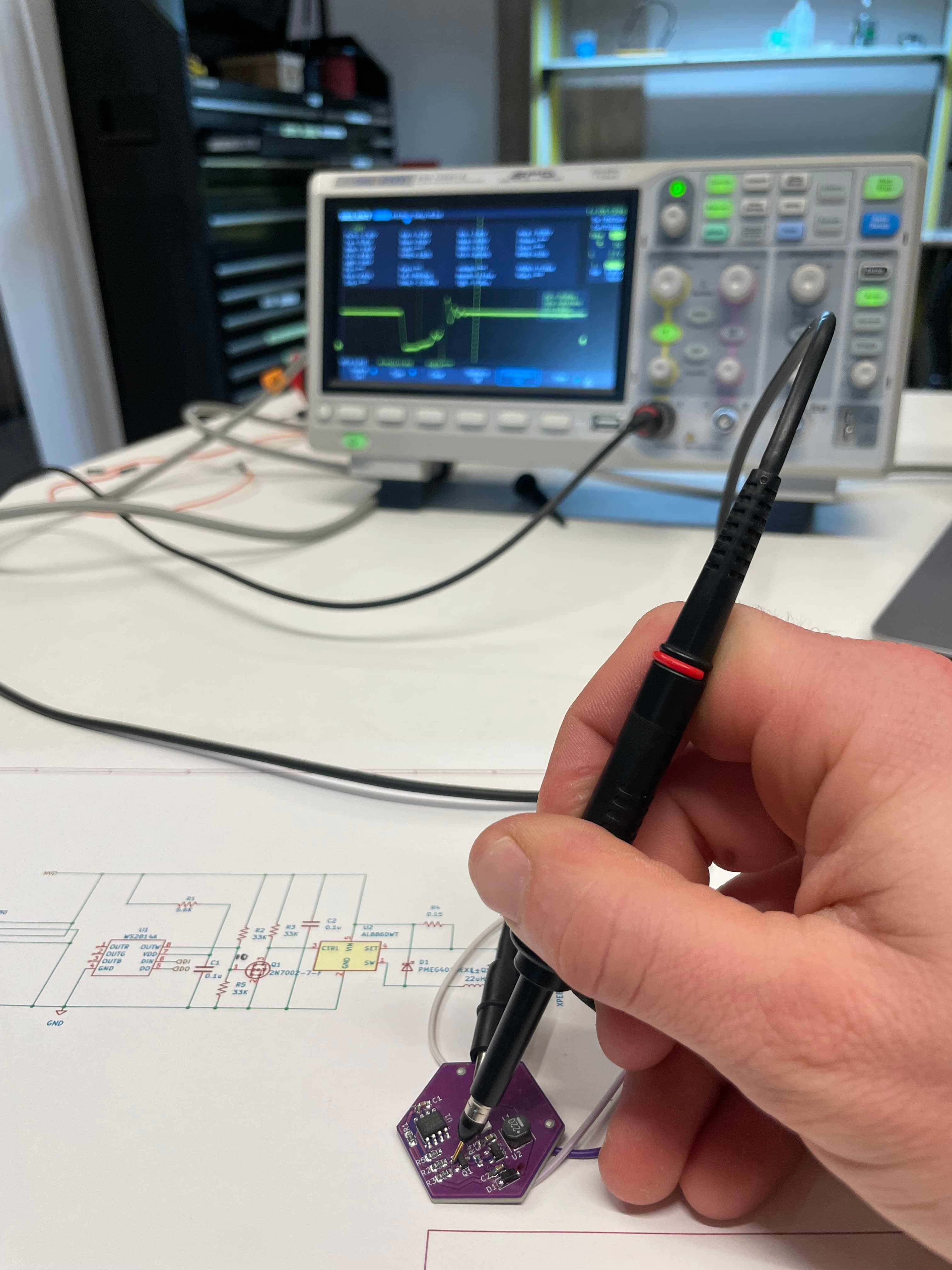 A hand probing a purple Sol Spektrum PCB with an oscilloscope, schematic visible on the workbench.