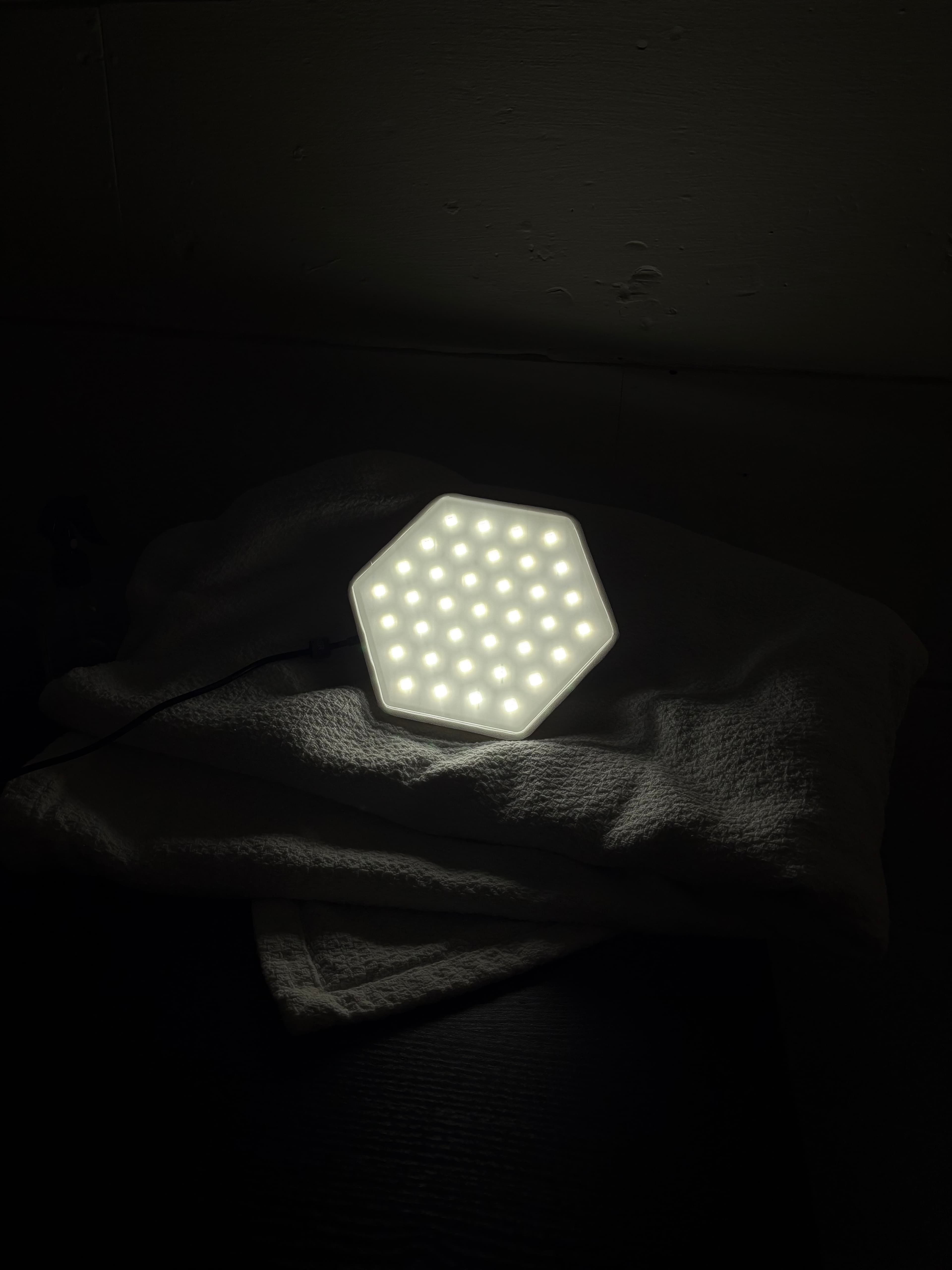 The finished Sol Spektrum hexagonal device lit warm white in a dark room.