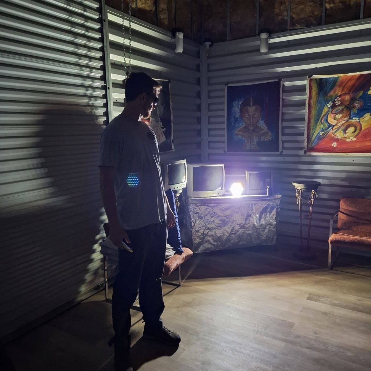 A person in a candle-lit room with vintage TVs and spiritual paintings, the Sol Spektrum device glowing on their chest.